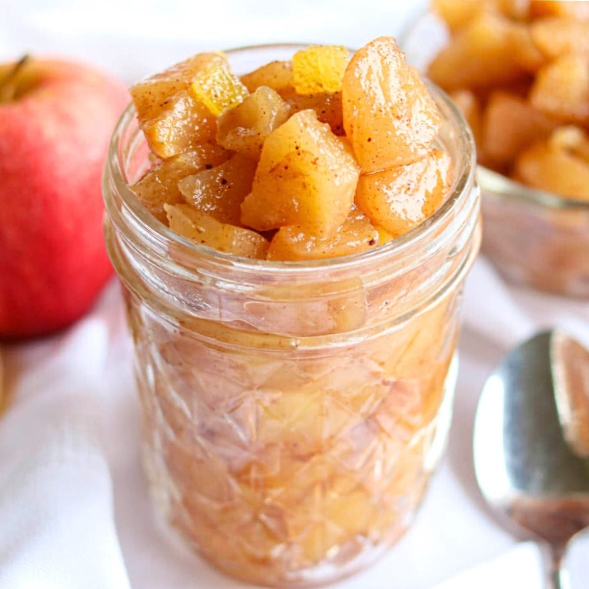 Closeup of apple compote in a glass jar on a white tablecloth.