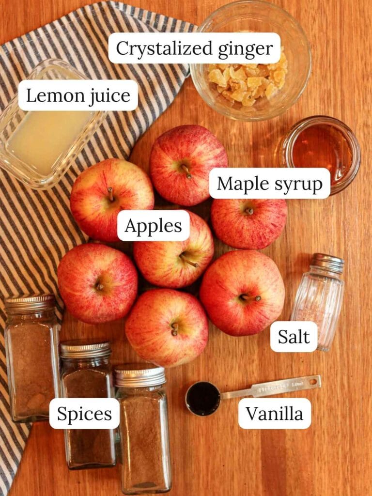 Labeled ingredients on a wood surface including apples, lemon juice, crystalized ginger, maple syrup, spices, salt, and vanilla.