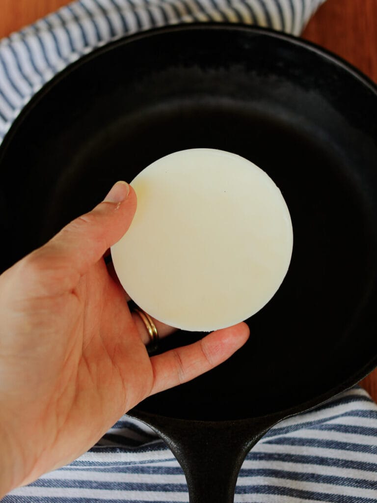 Hand holding a bar of cast iron seasoning wax over a skillet.