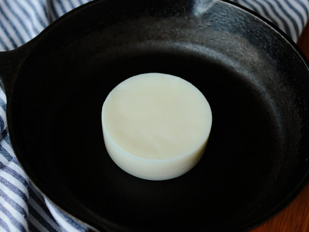 A white bar of cast iron seasoning wax in a large cast iron skillet.