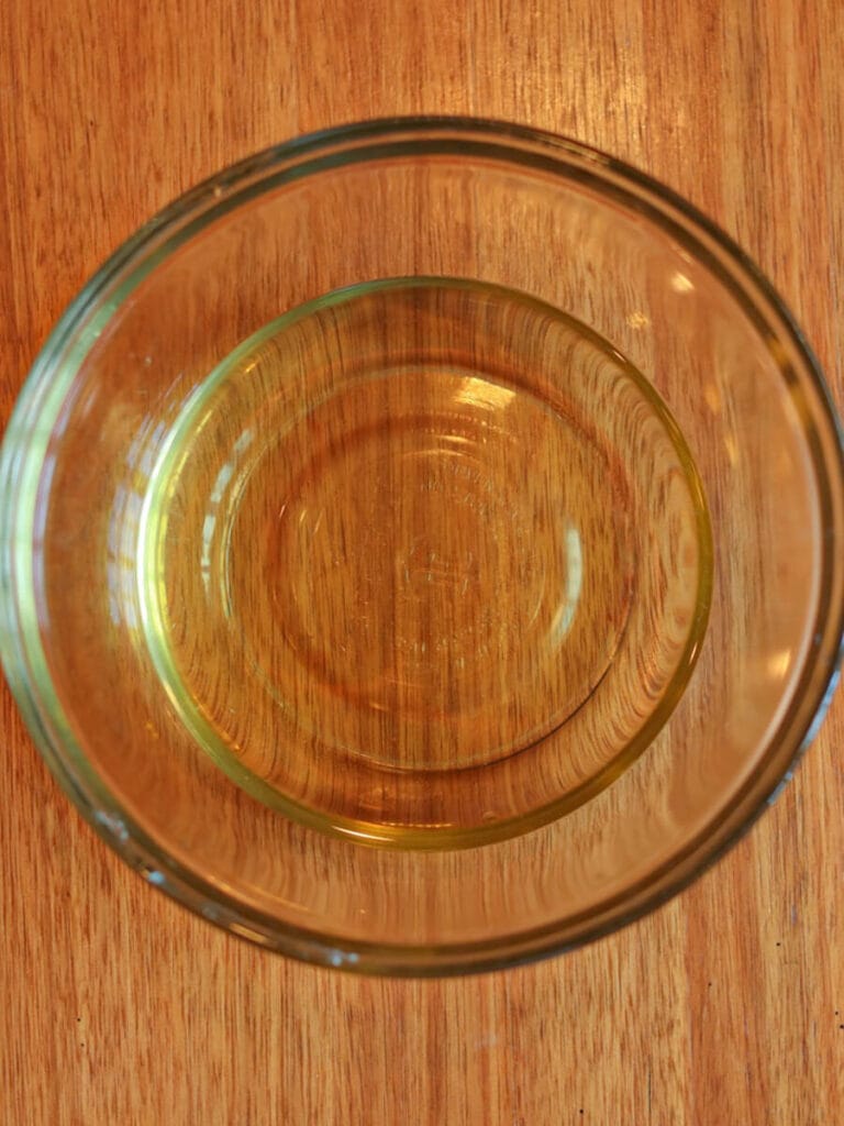 Melted beeswax, tallow, and avocado oil in a glass bowl on a wooden surface.
