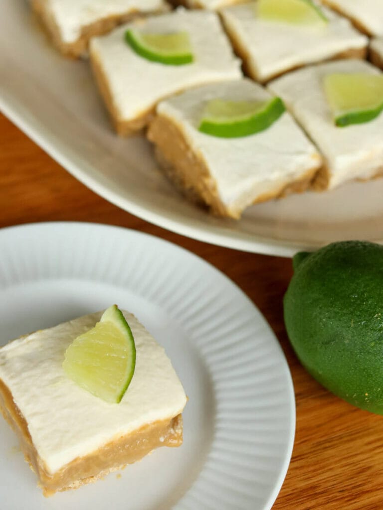 Gluten-free lime bars garnished with lime slices on a plate and serving platter on a wooden table.