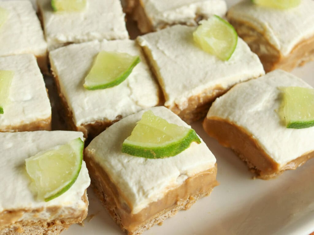 Gluten-free lime bars with lime curd and whipped cream on a tray.