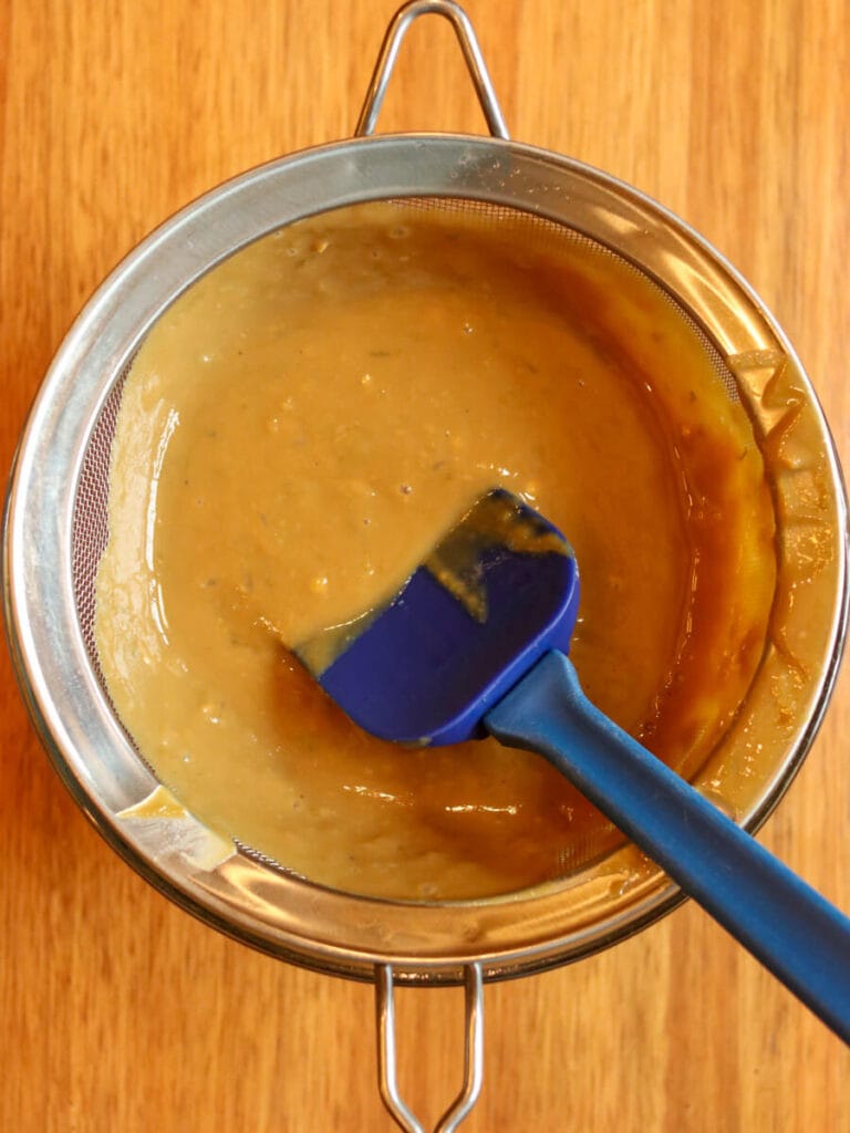 Lime curd being strained through a mesh strainer on a wooden surface.