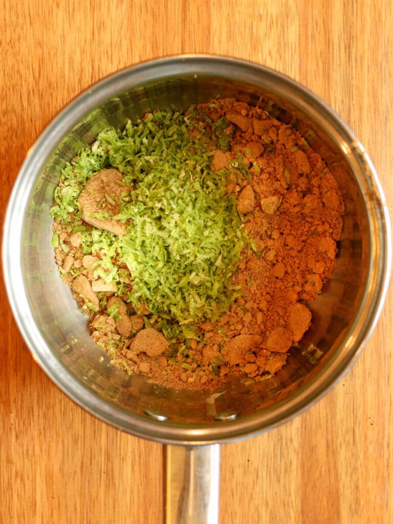 Coconut sugar and lime zest in a saucepan on a wooden surface.