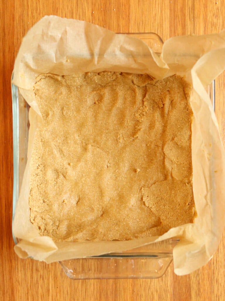 Oat shortbread batter pressed into a baking dish lined with parchment paper.