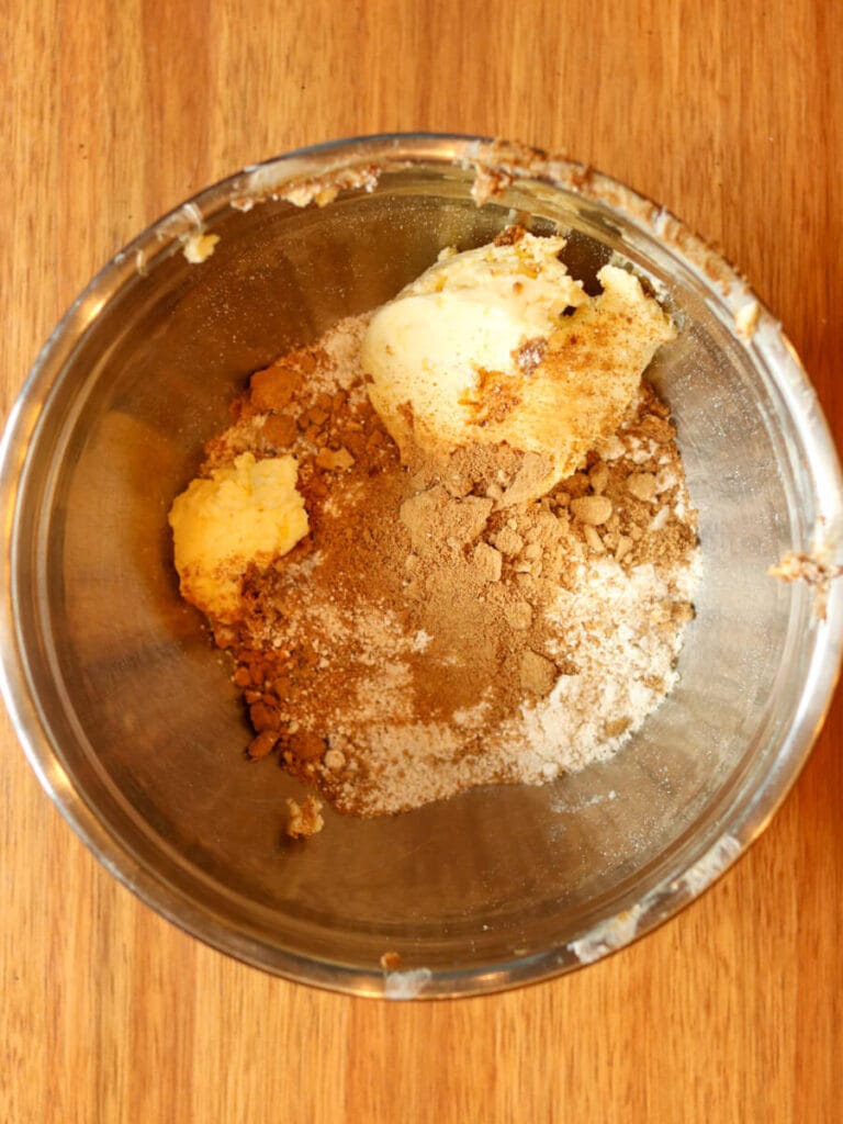 Mixing butter, sugar, oat flour, and other ingredients in a mixing bowl on a glass table.