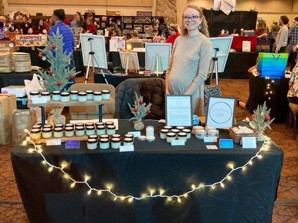 Woman standing behind a table at a market selling tallow skincare.