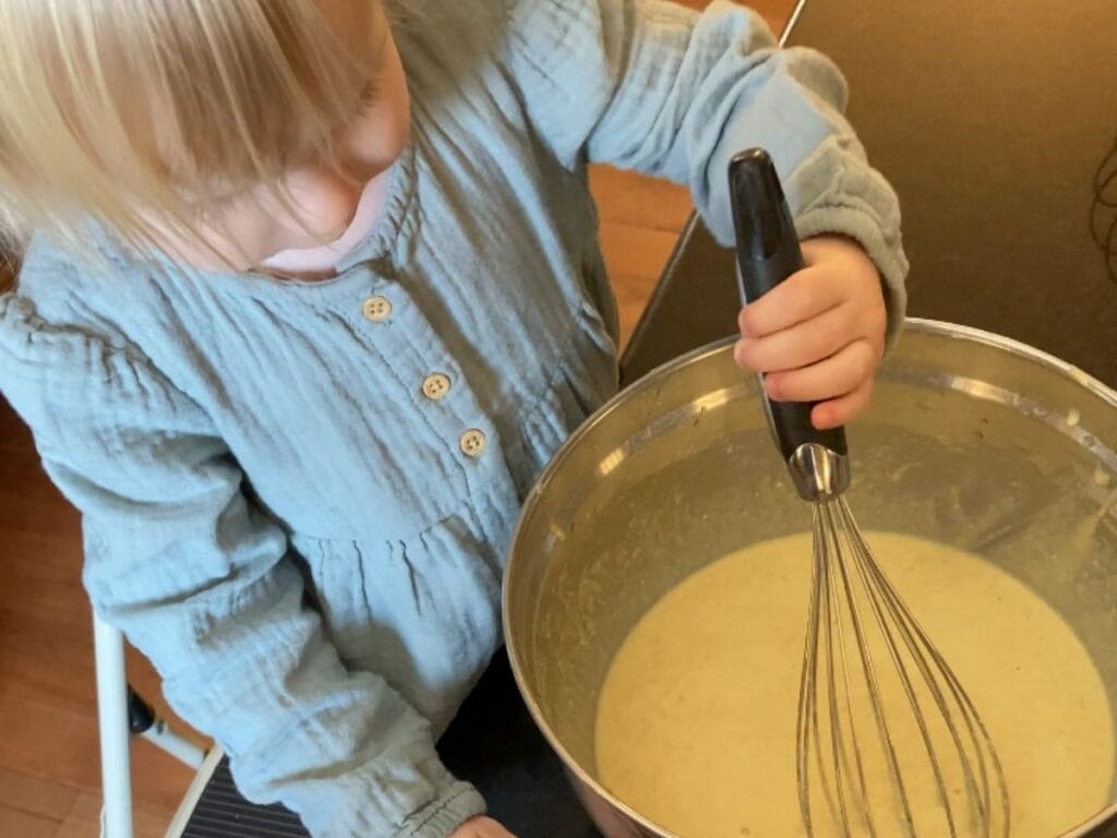 Toddler whisking pancake batter in a bowl.
