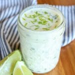 Closeup of lime crema topped with lime zest in a glass mason jar on a wooden table with fresh lime slices.