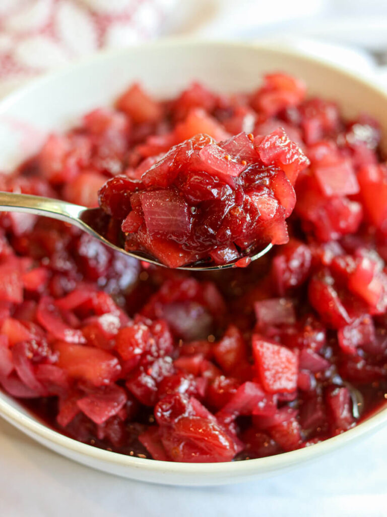 Spoon scooping apple cranberry chutney out of a white bowl.