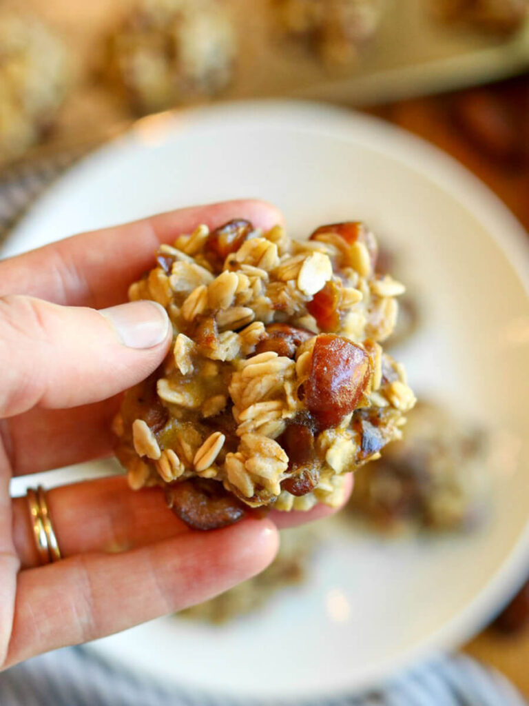 Hand holding a banana date oatmeal cookie above a plate of cookies.