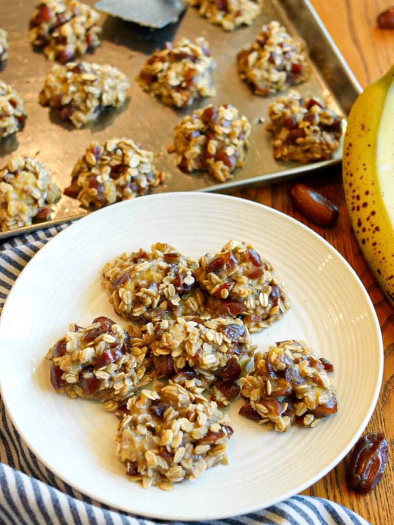 A plate of healthy banana date cookies with a pan of cookies in the background.