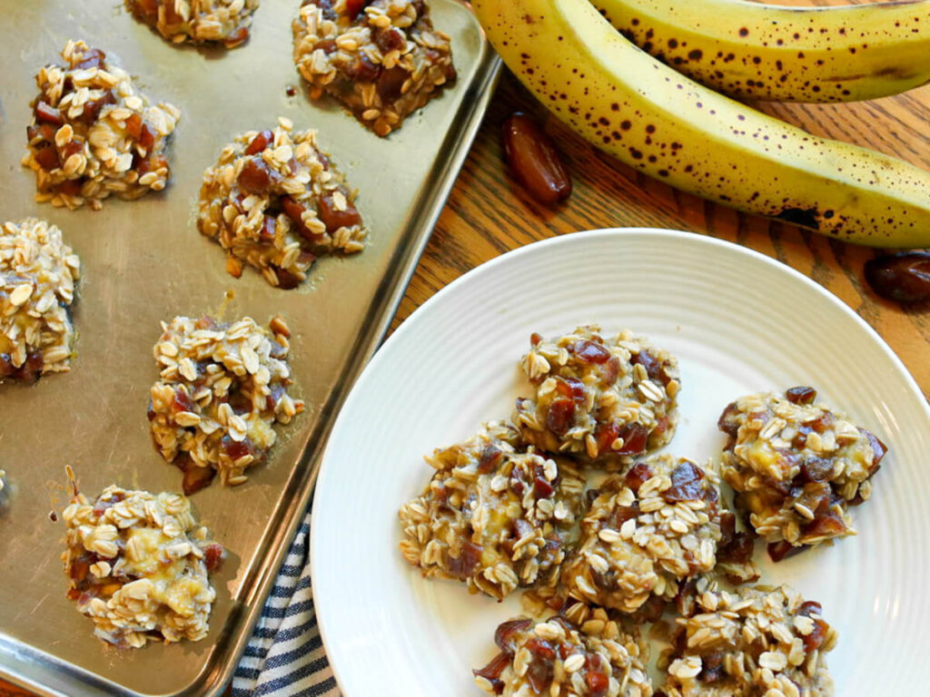 A plate of banana date oatmeal cookies beside pan of cookies.