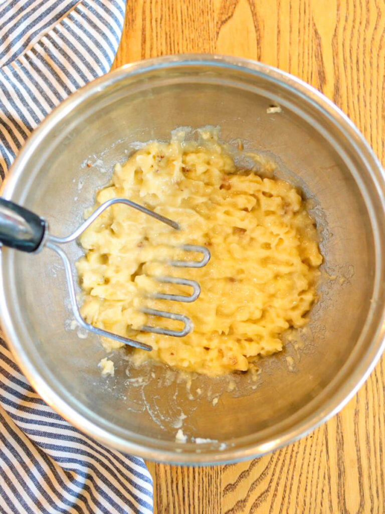 Mashing bananas in a stainless steel mixing bowl on a wooden table.