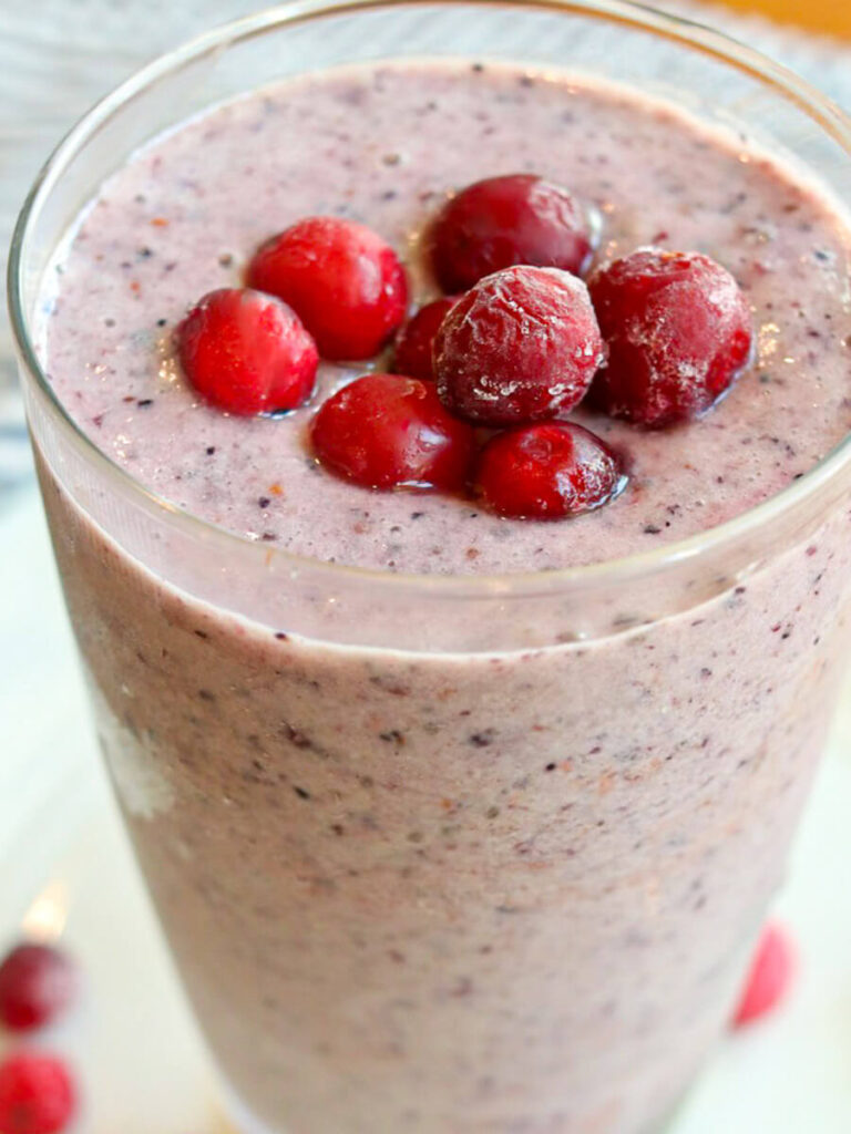 Close up view of a cranberry smoothie in a glass with frozen cranberries on top.