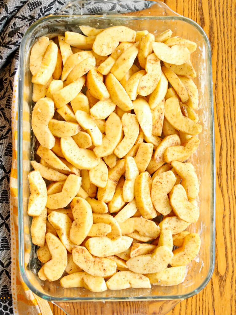 Spiced apple slices in a glass baking dish on a wood table.