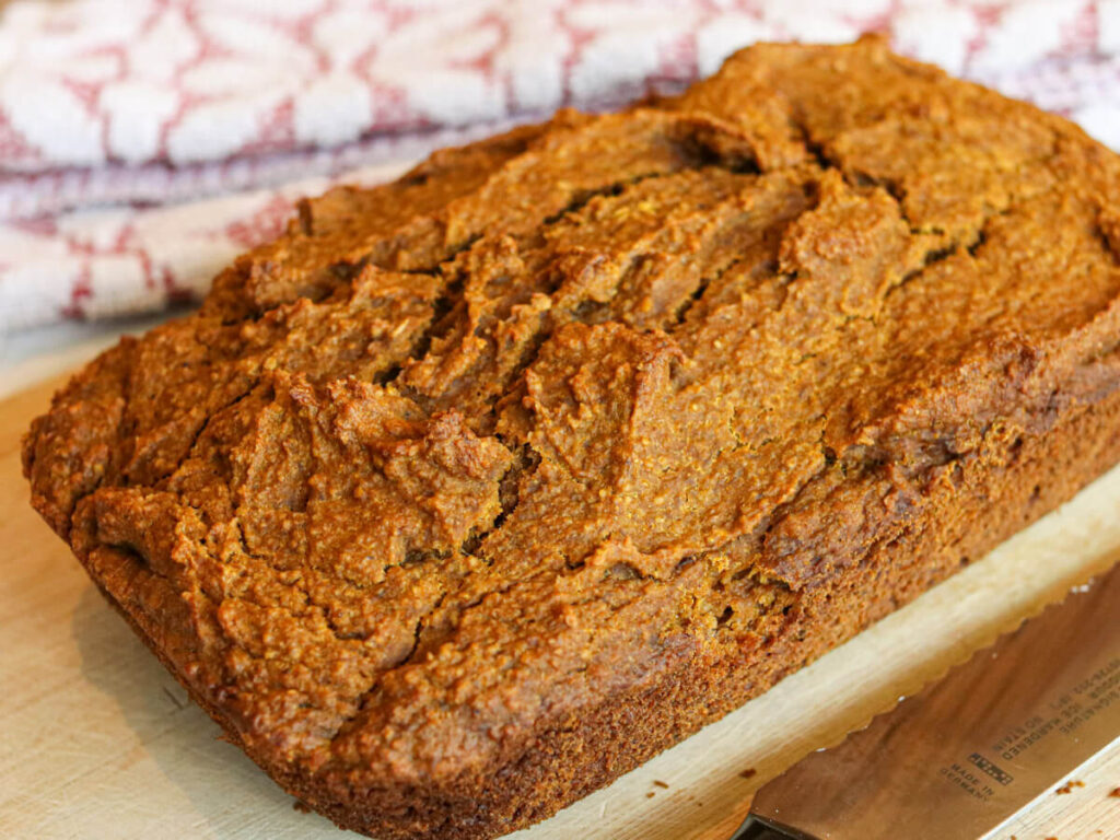 A loaf of healthy banana pumpkin bread on a wooden cutting board with a kitchen towel in the background.