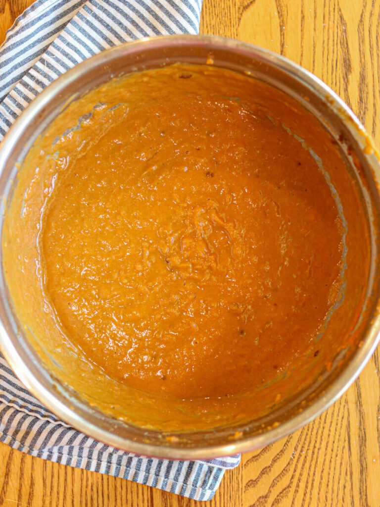 Pumpkin, mashed banana, and other wet ingredients mixed in a bowl on a wood table.