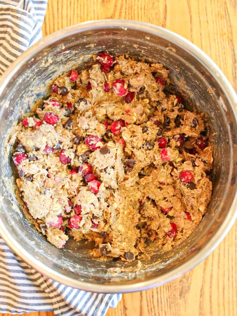 Cookie dough with lots of chocolate chips and cranberries in a metal bowl on a wooden table.