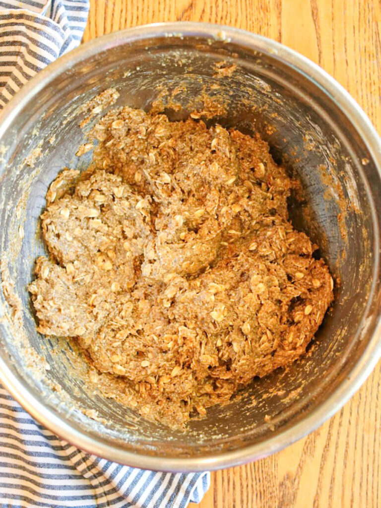 Oatmeal cookie batter mixed in a metal bowl on a wooden surface.