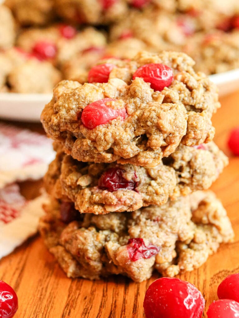 Stack of three oatmeal cranberry walnut cookies on a wooden table with more cookies in the background.