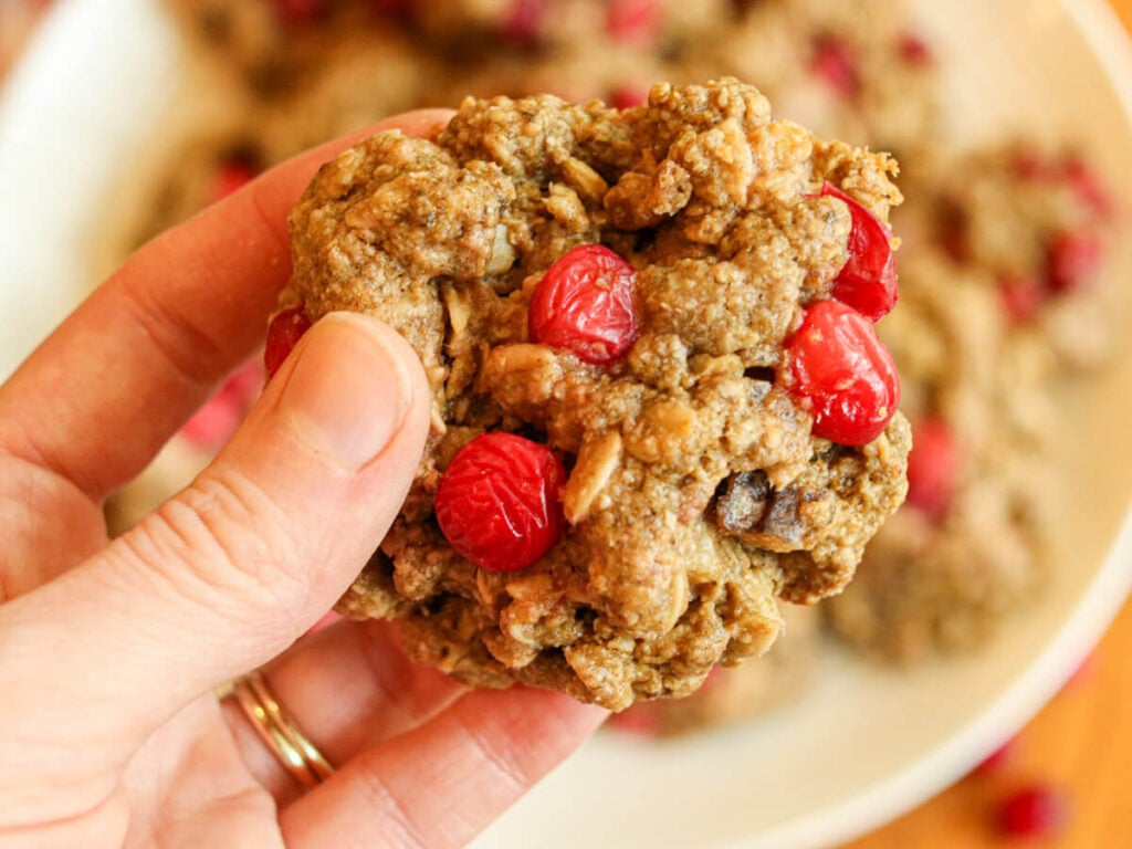 Hand holding a chunky cookie with cranberries over a plate of cookies.