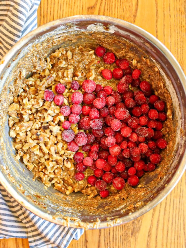 Walnuts and frozen cranberries added to a bowl of oatmeal cookie dough.