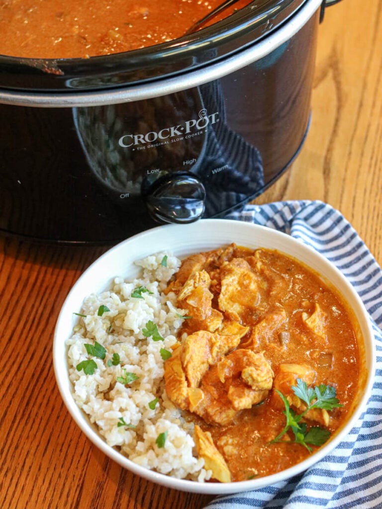 Chicken curry served in a bowl with rice with a slow cooker in the background.