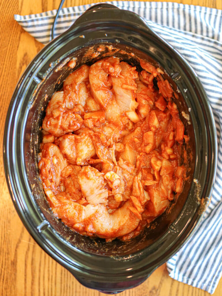 Chicken covered in sauce in a slow cooker ready to cook.