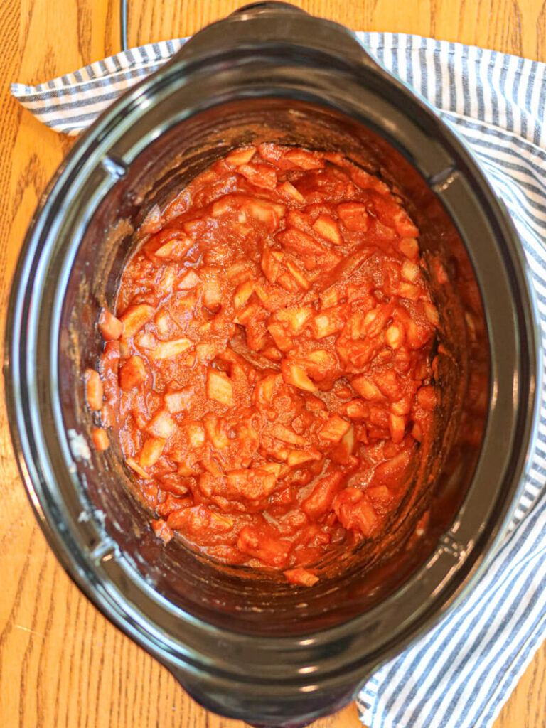 Tomato sauce, spices, chopped onion, and other ingredients in a slow cooker.