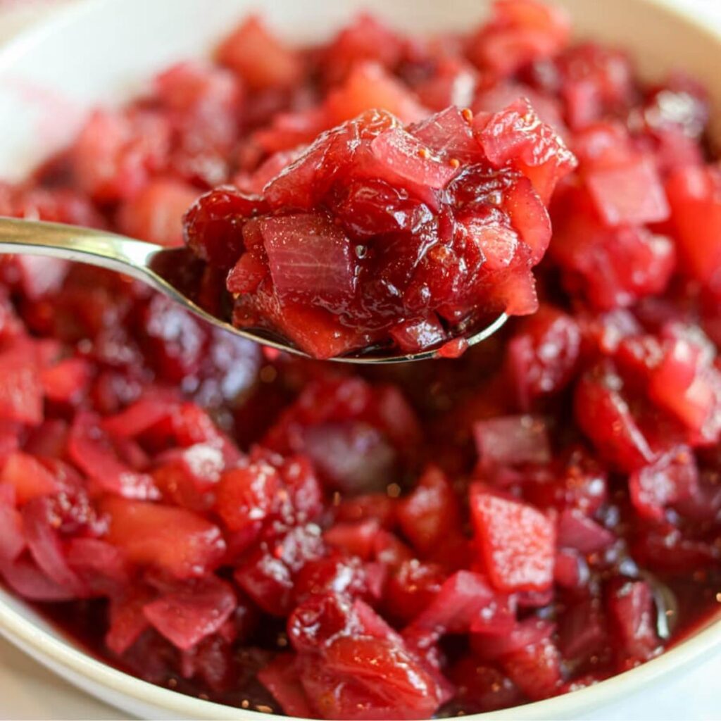 Closeup view of spoon scooping vibrant apple cranberry chutney out of a serving bowl.