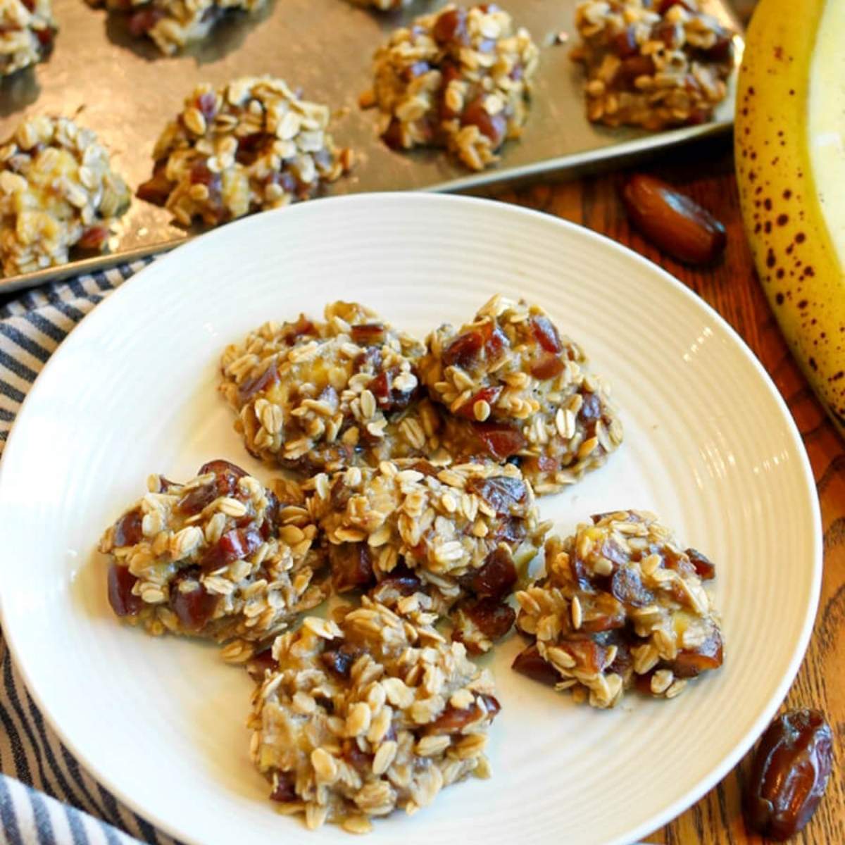 Banana date oatmeal cookies on a white plate with more cookies in the background.