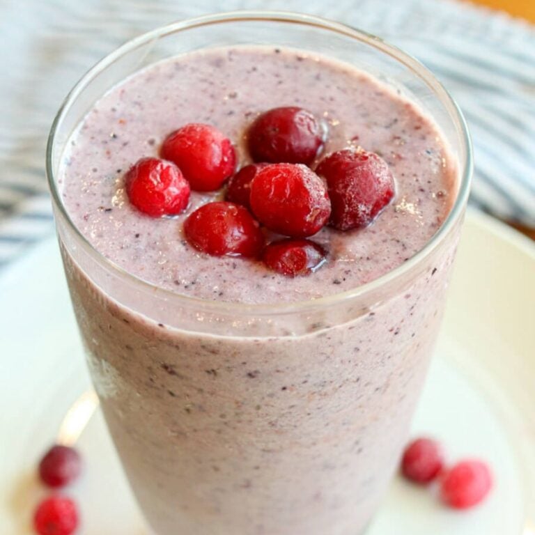 A bright cranberry smoothie in a drinking glass with additional cranberries on top.