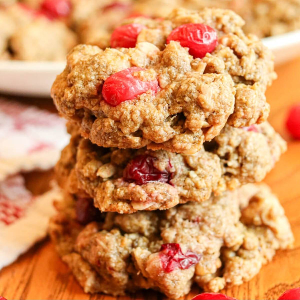Closeup of a stack of three cranberry walnut oatmeal cookies on a wooden table.
