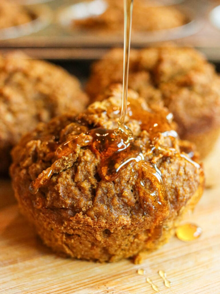 A banana pumpkin muffin on a cutting board being drizzled with honey.