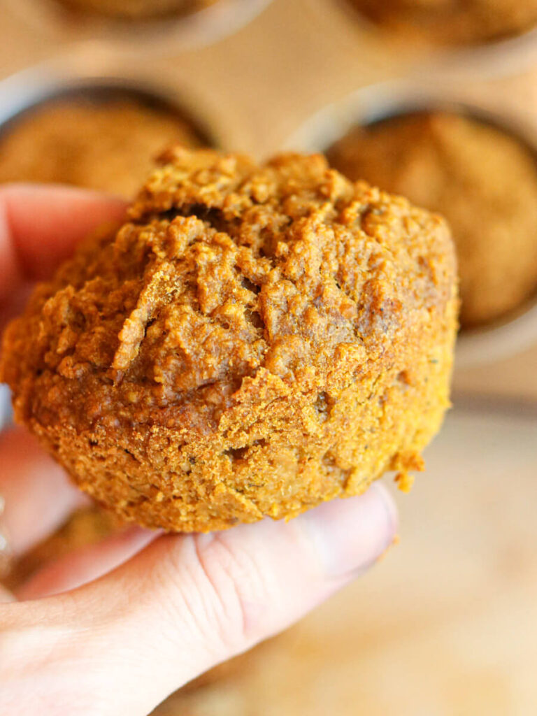 Hand holding a healthy banana pumpkin muffin over a muffin pan.
