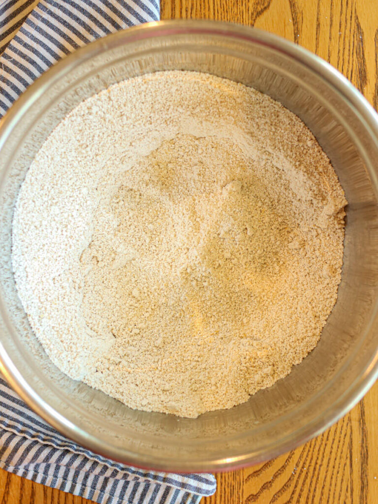 Oat flour and other dry ingredients combined in a mixing bowl on a wood table.