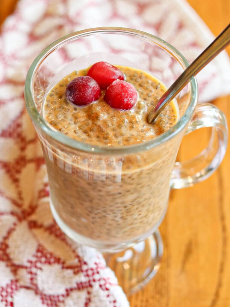 A glass of pumpkin chia seed pudding topped with cranberries with a spoon in it.