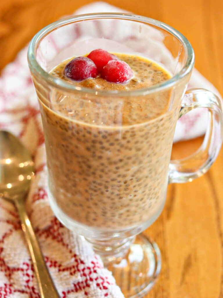 A serving glass full of chia seed pudding with pumpkin on a wooden table.