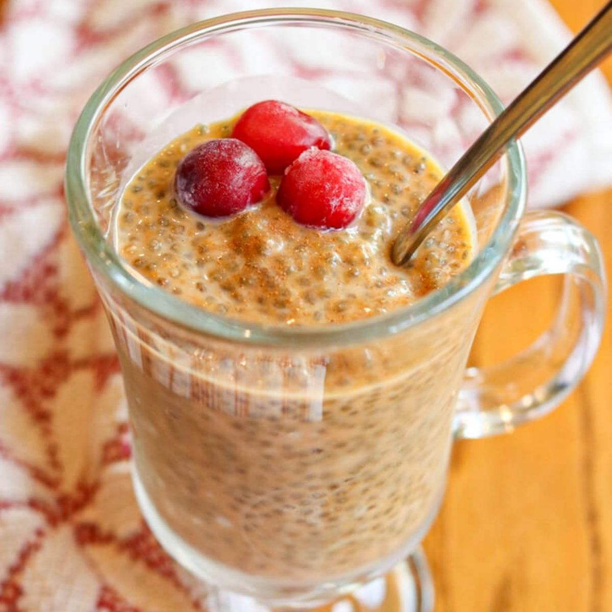 Closeup of pumpkin chia seed pudding in a glass with a spoon in it on a wooden table.
