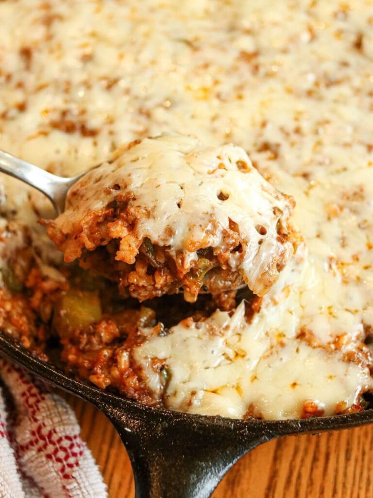 Spoon scooping deconstructed stuffed peppers with a cheesy topping out of a skillet.