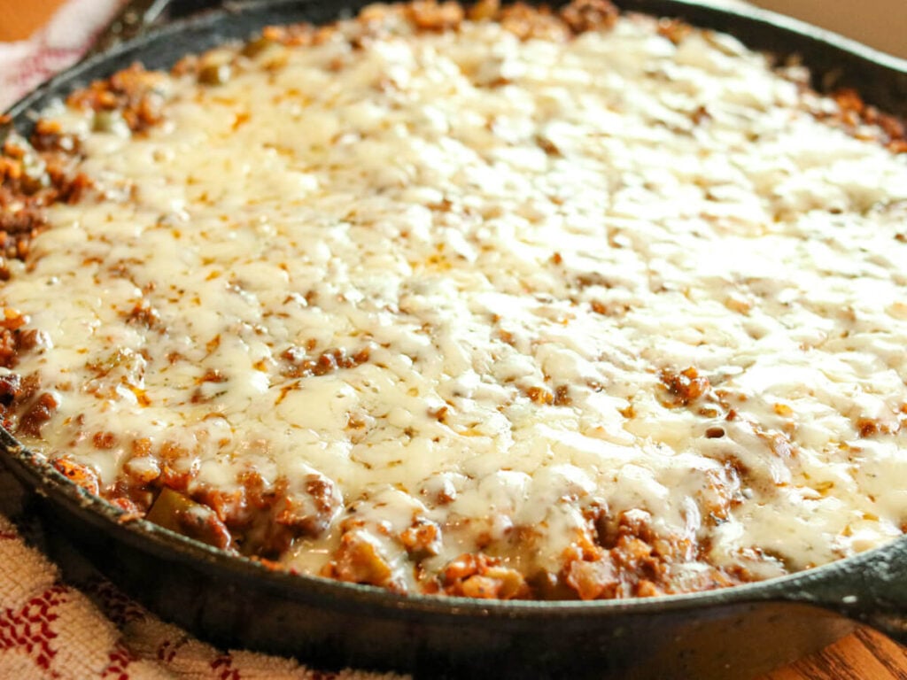 Side angle of a cast iron skillet full of unstuffed pepper casserole with a cheesy topping.