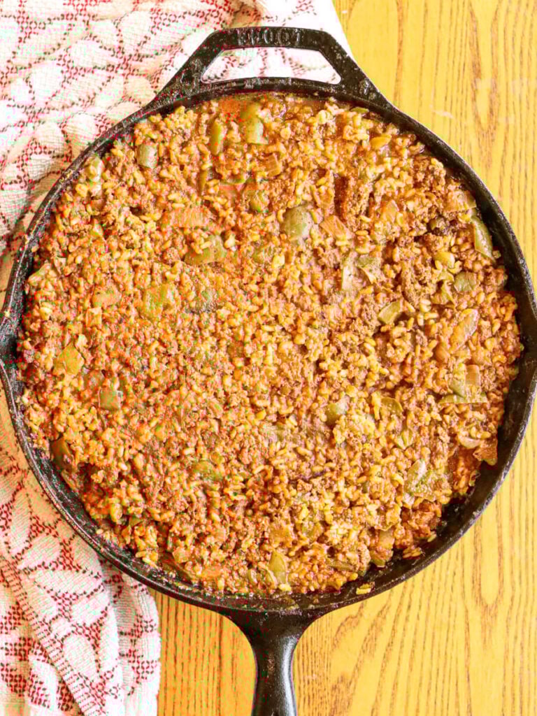 Ground beef, rice, and peppers in a tomato sauce in a skillet on a wooden table.