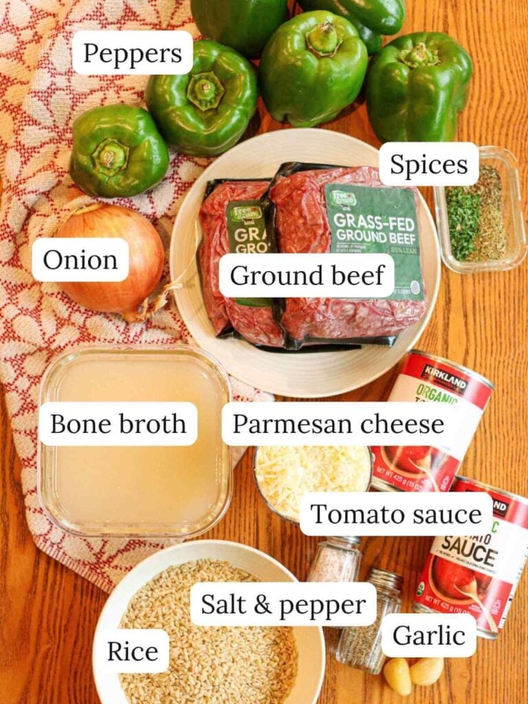 Labeled ingredients on a wooden table including peppers, ground beef, onion, cheese, bone broth, rice, tomato sauce, garlic, spices, salt and pepper.