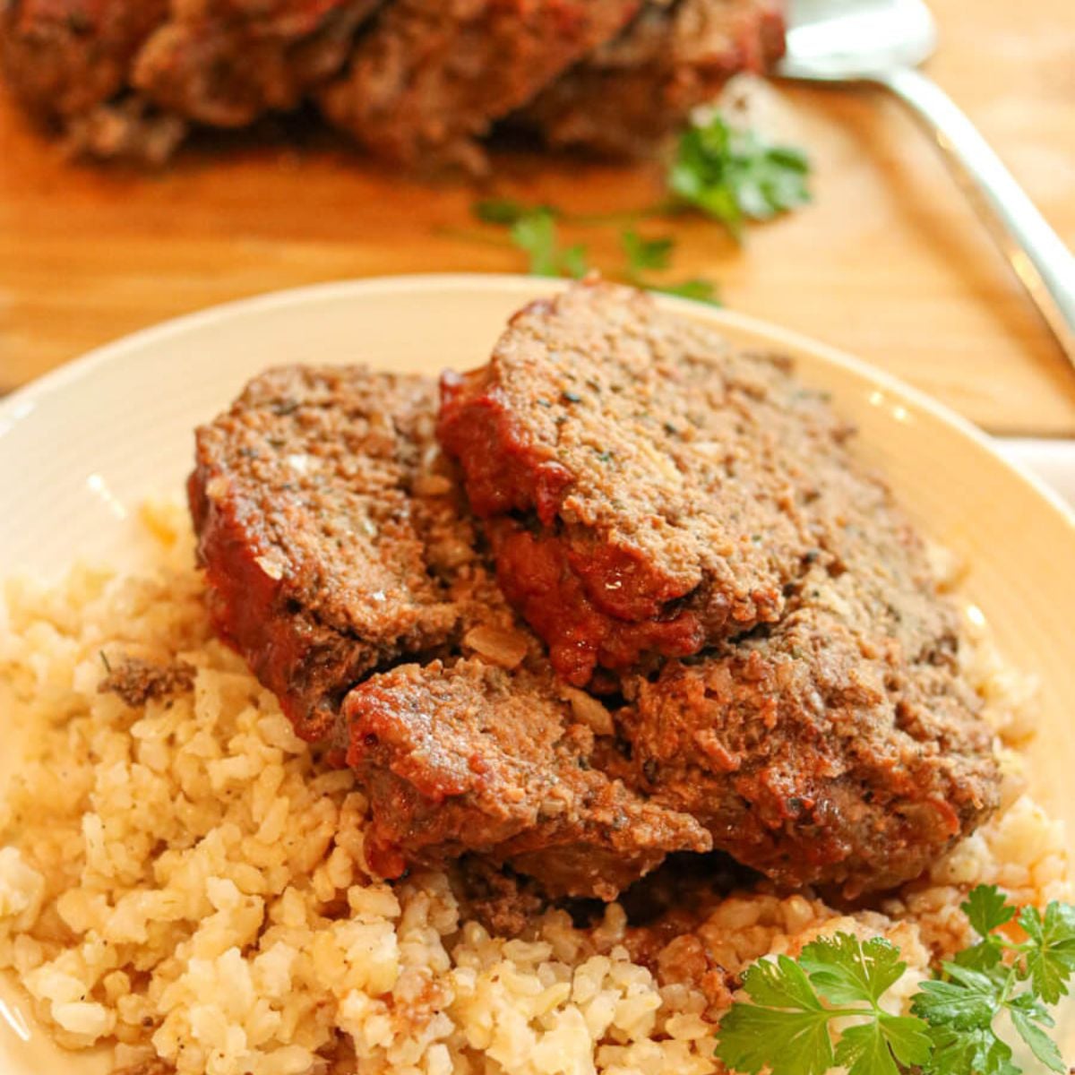 Closeup view of two slices of eggless meatloaf with rice on a plate garnished with fresh parsley.