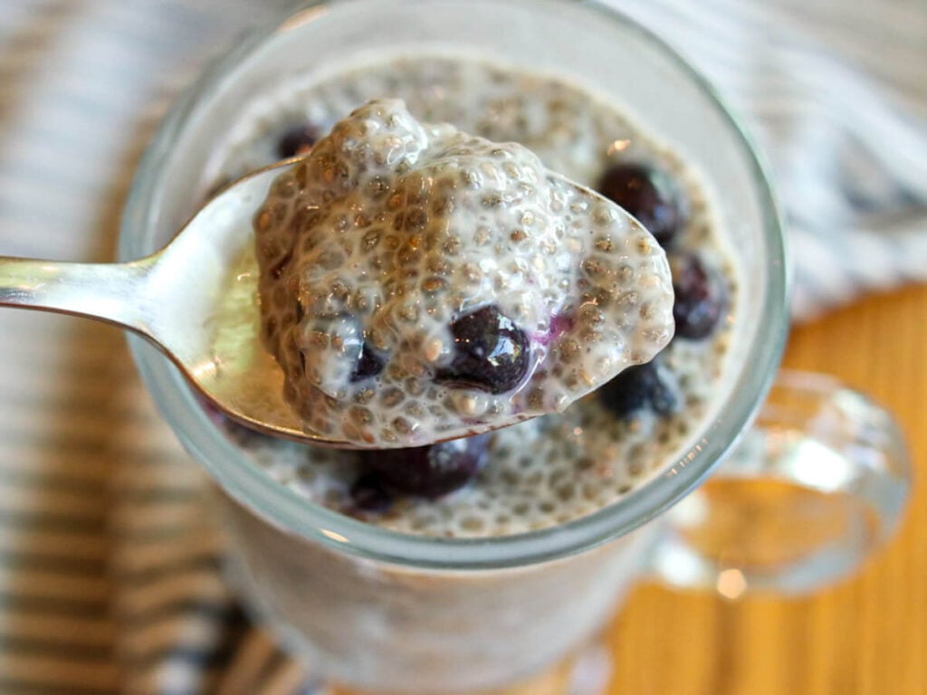 A spoon scooping a bite of blueberry chia pudding out of a glass.