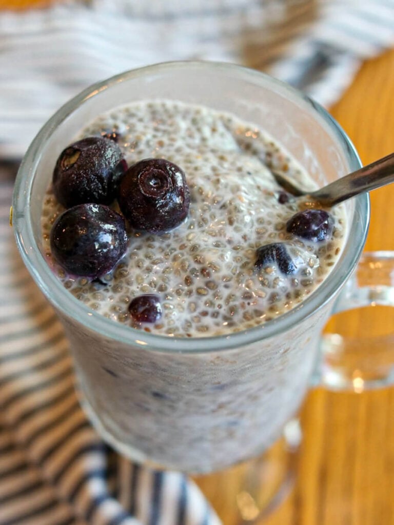 Blueberry chia seed pudding in a glass with a spoon in it on a wooden table.