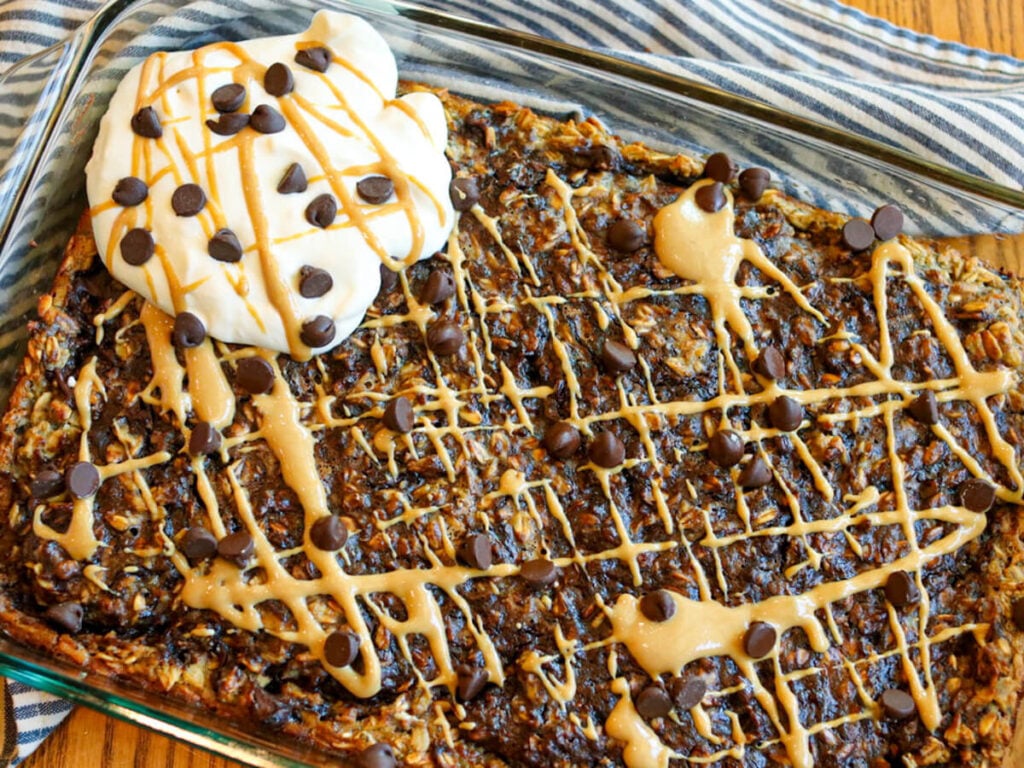 Chocolate baked oats with peanut butter in a baking dish served with whipped cream and drizzled with peanut butter.