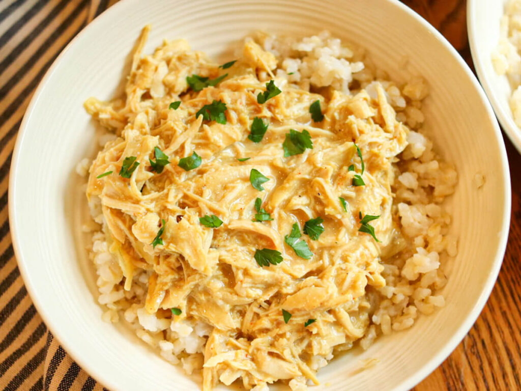 A bowl full of crockpot honey mustard chicken garnished with fresh parsley served over rice.